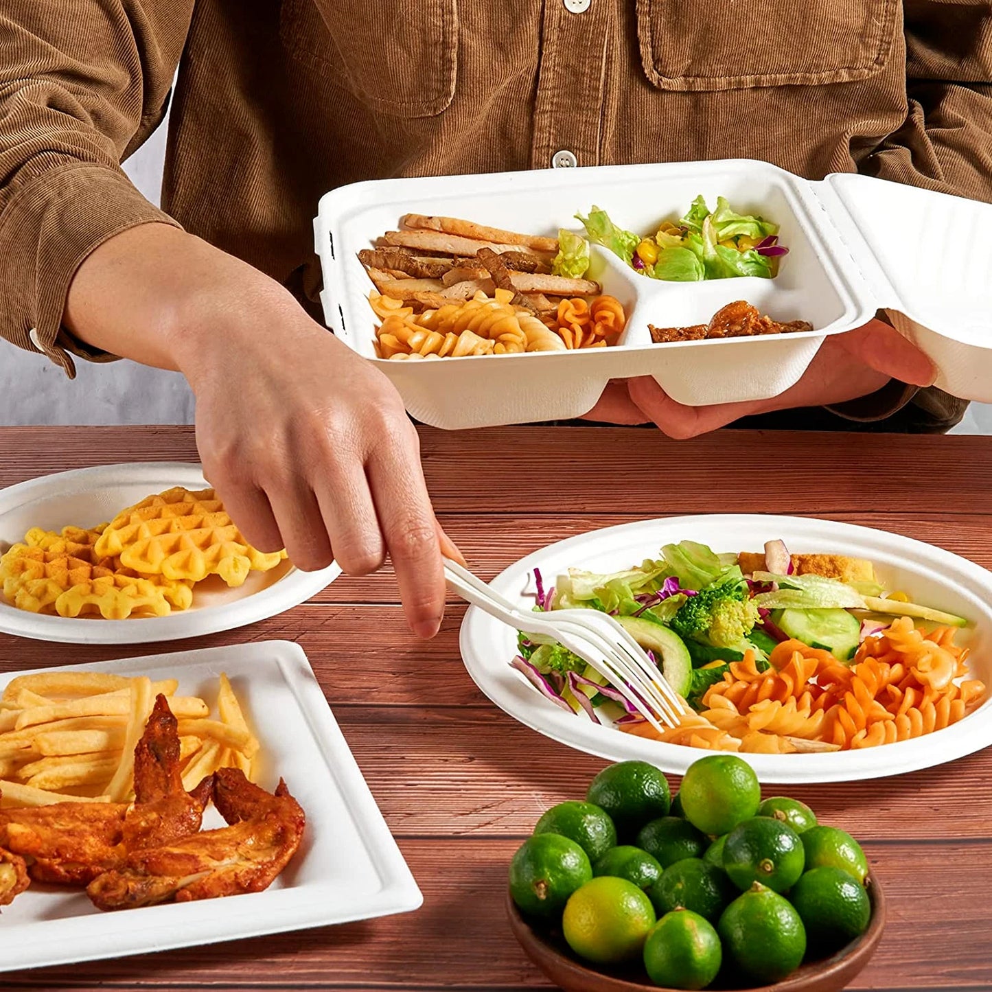Person pointing at a plate of food with various dishes including salad, fries, and waffles on a wooden table.