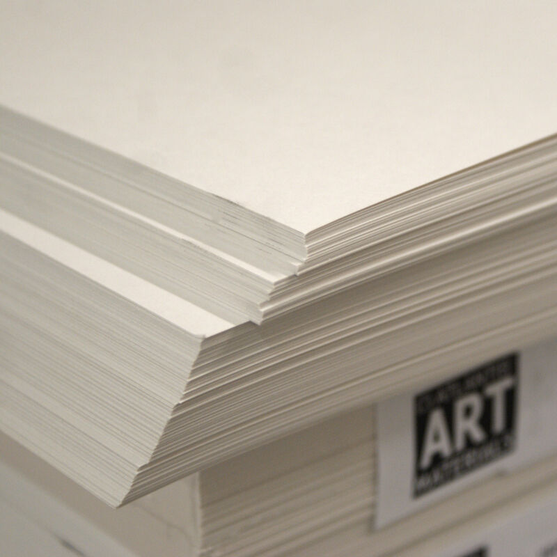 Stack of white cartridge paper sheets, A2 size, bound together with a rubber band, on a desk.
