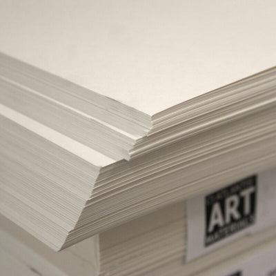 Stack of white cartridge paper sheets, A2 size, bound together with a rubber band, on a desk.