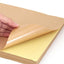 A stack of brown A4 kraft self-adhesive sticker paper sheets with one sheet partially lifted to show the adhesive side.