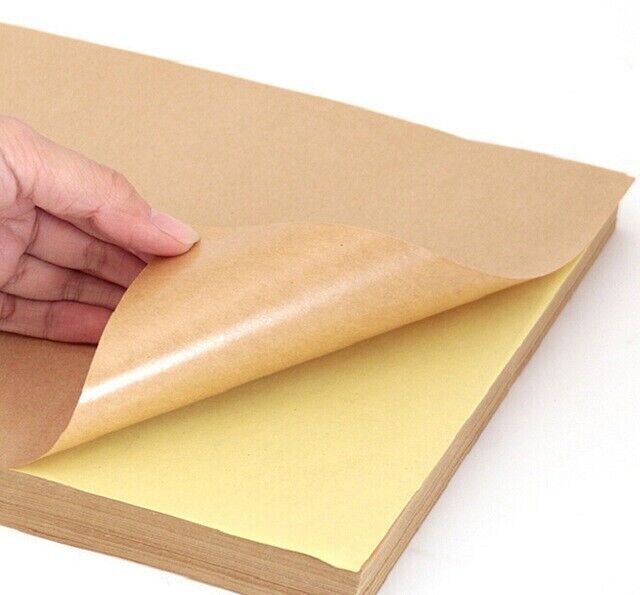 A stack of brown A4 kraft self-adhesive sticker paper sheets with one sheet partially lifted to show the adhesive side.