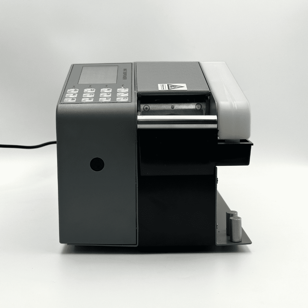 A compact industrial label printer or barcode scanner with a dark gray and black body, featuring a control panel with buttons on the left, a paper slot in the center, and a light gray cover on the right, photographed on a light gray studio background.