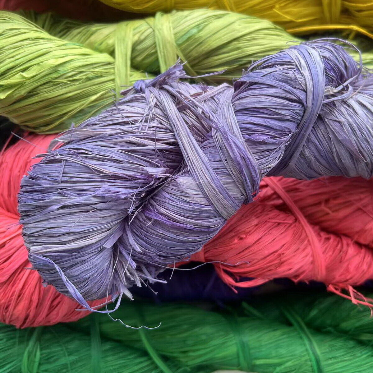 A collection of colorful raffia hanks, arranged in a pile with shades including purple, red, green, yellow, and blue.