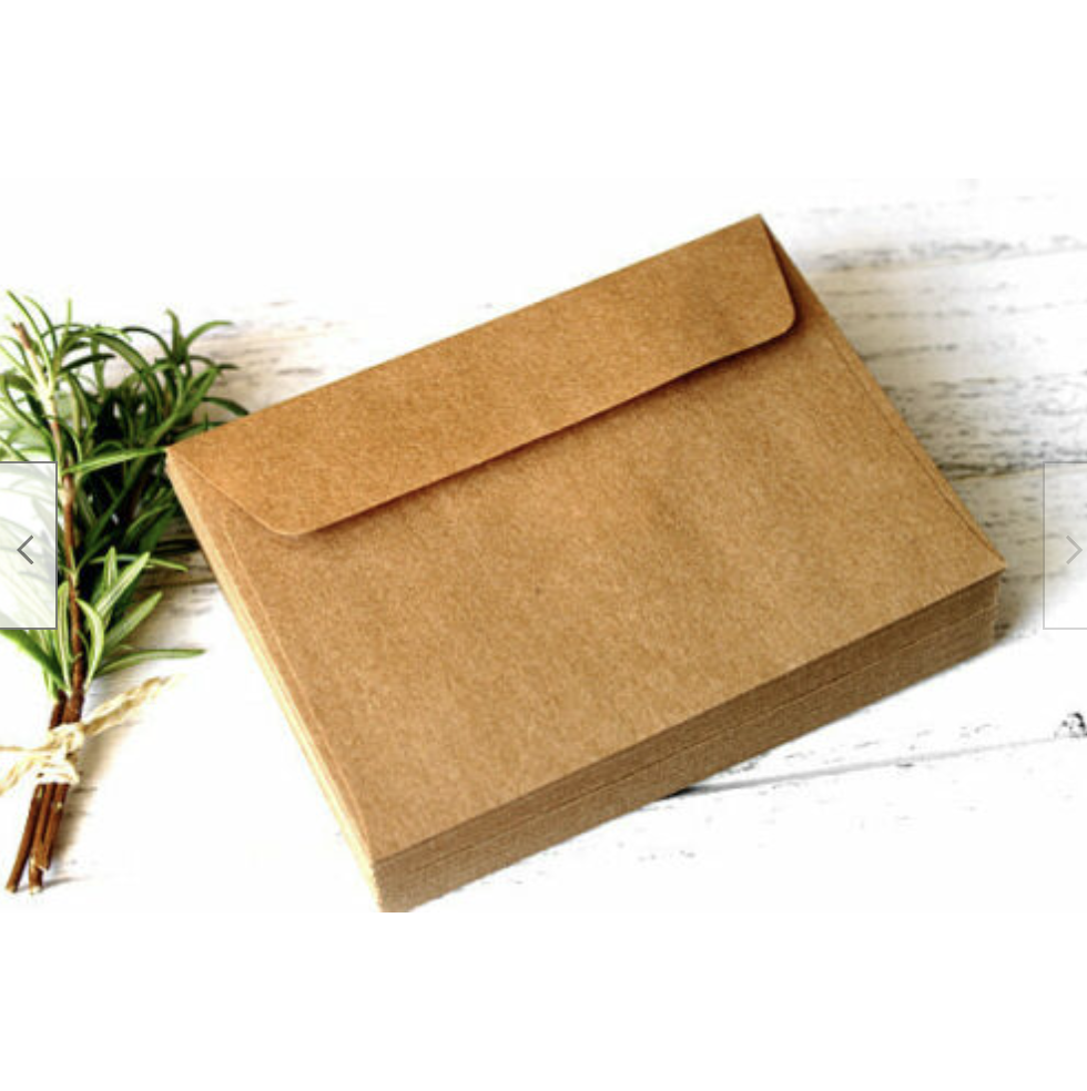A stack of brown kraft envelopes displayed on a surface with a sprig of herbs to the side.