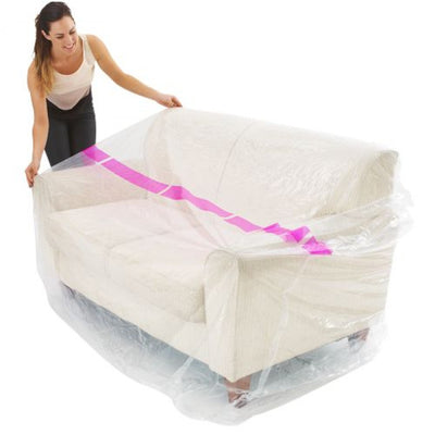 A person is covering a couch with a white plastic furniture cover, which is translucent and seems to be the product in question.